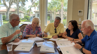 A Florida HOA board reviewing management company proposals together at a community clubhouse table.